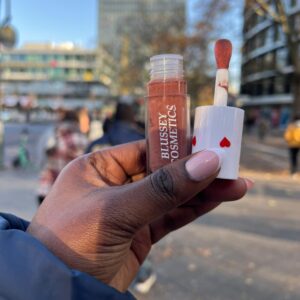 A female hand holding the dew lip gloss in an outdoor setting