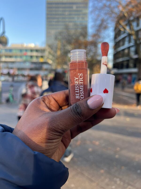 A female hand holding the dew lip gloss in an outdoor setting