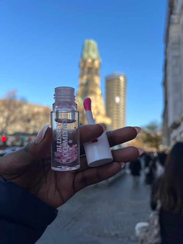 A female hand holding the sweet melody lip gloss in an outdoor setting